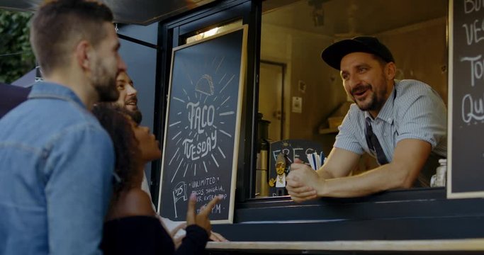 Cheerful waiter taking order from multi-racial customers at counter, Mexican street food served from a food truck. 4K UHD RAW graded footage