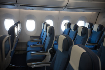 An economy class empty clean cabin of the airplane - empty dark blue chairs - opened portholes