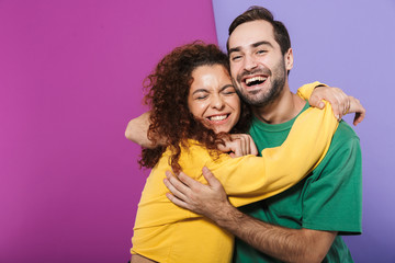 Portrait of excited caucasian couple man and woman in colorful clothing rejoicing and hugging together