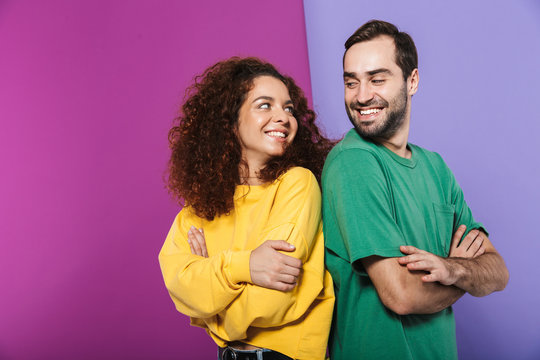 Portrait of brunette caucasian couple man and woman in colorful clothing smiling at each other standing with arms crossed