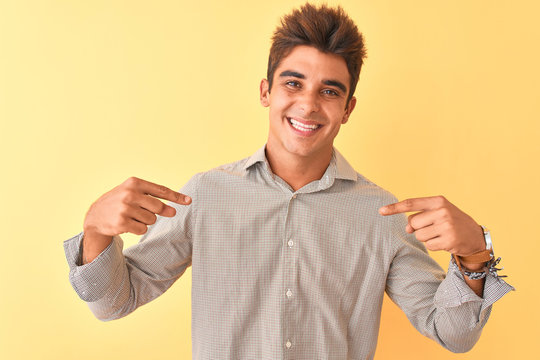 Young handsome man wearing casual shirt standing over isolated yellow background looking confident with smile on face, pointing oneself with fingers proud and happy.