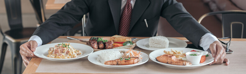 Man eating lots of food on the table with fired fish, pork steak, steam cooking rice, health care concept.