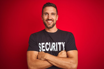 Young safeguard man wearing security uniform over red isolated background happy face smiling with crossed arms looking at the camera. Positive person.