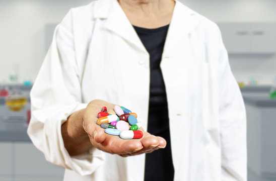 Old woman doctor holding pills, capsules, drugs and medics on a blurred laboratory background 3d rendering. Medicine, health care, overmedication and disease healing concept.