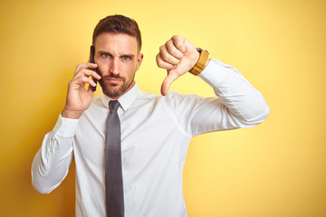 Young handsome business man talking on the phone over yellow isolated background with angry face,...