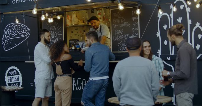 Cheerful waiter taking order from multi-racial customers at counter, Mexican street food served from a food truck. 4K UHD RAW graded footage