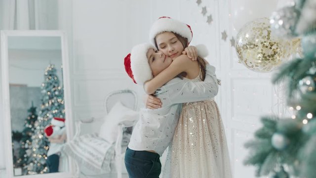 Smiling children hugging each other near chritmas tree.