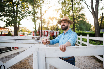 A portrait of farmer walking outdoors on family farm, opening gate.