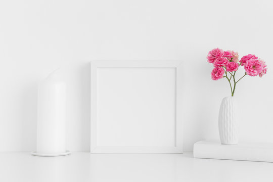 White square frame mockup with pink roses in a vase and workspace accessories on a white table.