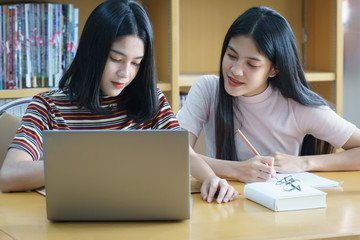 Young Asian woman student study and take notes with book in library. F