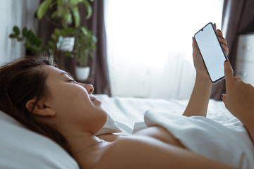 woman with smartphone in bed with white sheets
