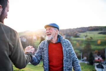 Laughing senior father and his son on walk in nature, shaking hands.