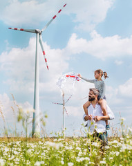 Mature father with small daughter walking on field on wind farm.