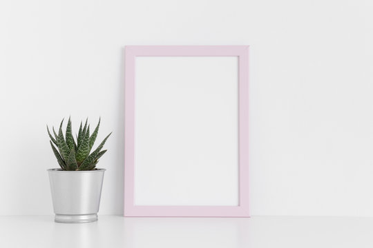 Pink frame mockup with a cactus in a pot on a white table. Portrait orientation.