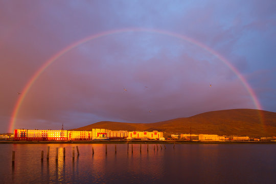 Beautiful cityscape with a rainbow over the lake, buildings and hills. Summer evening in the Arctic. Pevek, Chukotka, Siberia, Russian Far East. Polar region. Pevek is the northernmost city in Russia.