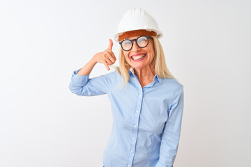 Middle age architect woman wearing glasses and helmet over isolated white background smiling doing phone gesture with hand and fingers like talking on the telephone. Communicating concepts.