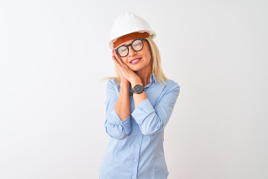 Middle age architect woman wearing glasses and helmet over isolated white background sleeping tired dreaming and posing with hands together while smiling with closed eyes.
