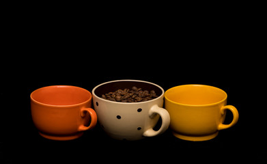 Coffee beans spread around coffee mugs on a black background