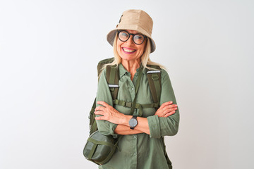 Fototapeta premium Middle age hiker woman wearing backpack hat canteen glasses over isolated white background happy face smiling with crossed arms looking at the camera. Positive person.
