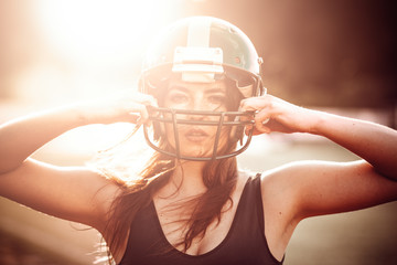 Sexy young sportive girl in uniform of rugby football player in action on the stadium. American football woman player stay on pitch, and hold helmet with sunlight