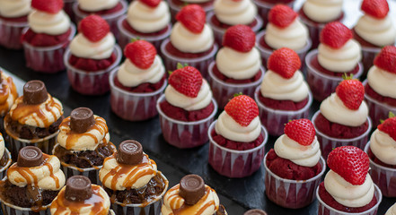 Fresh made red velvet and chocolate with caramel cupcakes with cream and strawberries on the top. 