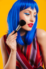 Portrait of seductive alluring woman wearing blue wig looking aside and applying powder with brush
