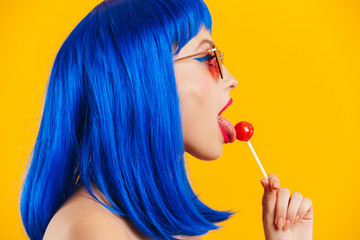Portrait in profile of glamorous nice young woman wearing blue wig and sunglasses licking lollipop - obrazy, fototapety, plakaty