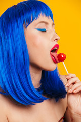 Portrait in profile of sexual nice young woman wearing blue wig licking lollipop with eyes closed