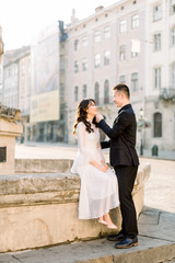 Stylish beautiful couple Asians newlyweds walking on the old city center streets on a sunny day of their wedding. Woman in white dress and man in black suit looking each other