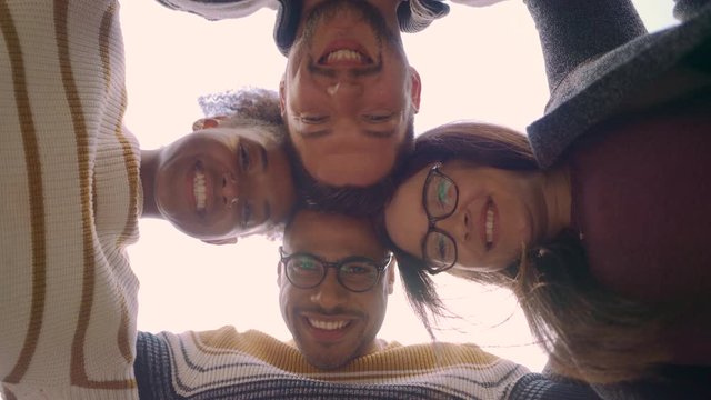 Low angle view of diverse young friends smiling and hugging with their heads together forming huddle