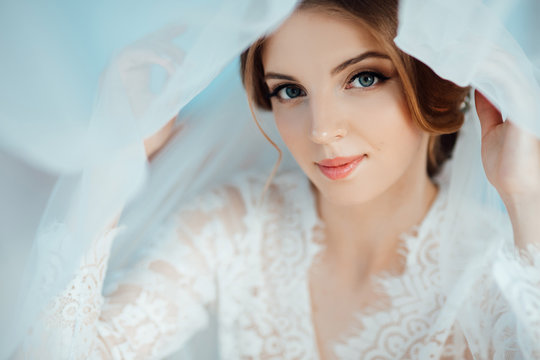 Gorgeous, elegant, fashion sexy bride wear white wearing robe. Stylish happy bride posing under veil and smiling.  Makeup and hairstyle in bride. Amazing bride in the morning preparation. 