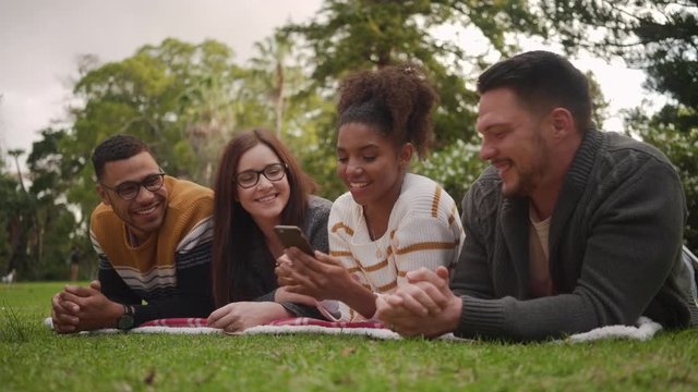 Smiling young african woman lying with her multiracial friends in the park taking selfie on mobile phone