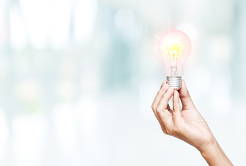 Woman hand holding light bulb in blurred background, Concept conveys ideas
