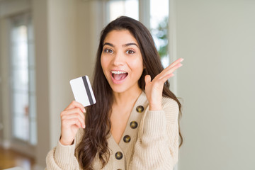 Young woman holding credit card as payment very happy and excited, winner expression celebrating victory screaming with big smile and raised hands