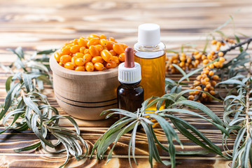 Organic sea buckthorn oil in the bottle with fresh sea buckthorn fruits and leaves on light stone...