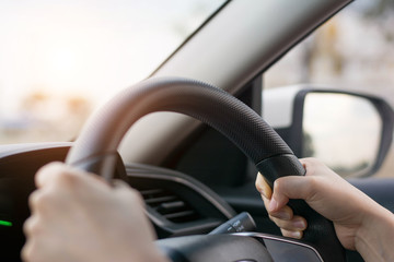 Female hands on the steering wheel of a car while driving. Against the background, the windshield and road,Close-up of a woman's hand driving a car