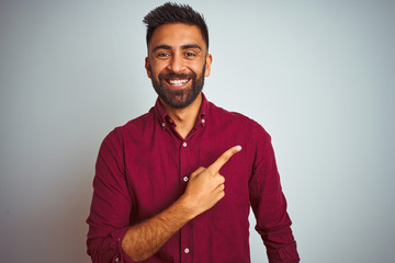 Young indian man wearing red elegant shirt standing over isolated grey background cheerful with a smile on face pointing with hand and finger up to the side with happy and natural expression - Powered by Adobe