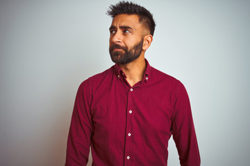 Young indian man wearing red elegant shirt standing over isolated grey background smiling looking...