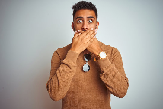 Indian man wearing elegant sweater and sunglasses standing over isolated white background shocked covering mouth with hands for mistake. Secret concept.