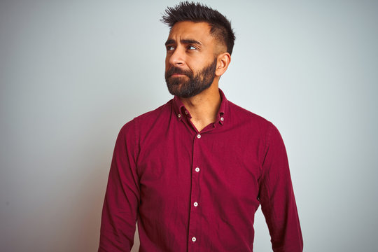 Young indian man wearing red elegant shirt standing over isolated grey background smiling looking to the side and staring away thinking.