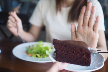 The girl is pushing the chocolate cake out. And choose to eat salad vegetables placed in front. The goal is to lose weight and eat healthy food.