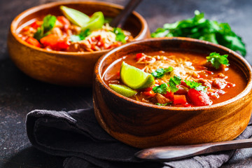 Traditional mexican bean soup with meat and cheese in wooden bowl, dark background. Mexican food...