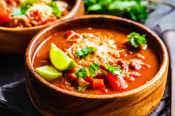 Traditional mexican bean soup with meat and cheese in wooden bowl, dark background. Mexican food concept.