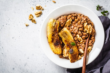 Chocolate oatmeal porridge with fried banana and walnut in white plate.