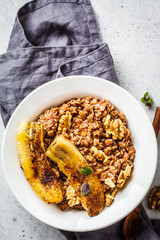 Chocolate oatmeal porridge with fried banana and walnut in white plate.