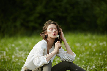 Portrait of a girl sitting in a field on the spring grass among dandelion flowers. Cheerful girl enjoys Sunny spring weather. Natural beauty of a woman, natural cosmetics