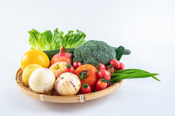 A bamboo plate filled with fresh seasonal vegetables and fruits on a white background