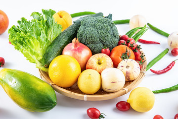 A bamboo plate filled with fresh seasonal vegetables and fruits on a white background