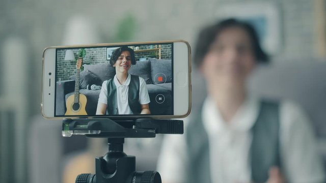 Portrait of happy teen recording video for vlog with smartphone talking gesturing looking at camera, focus on smart phone screen. Youth and equipment concept.