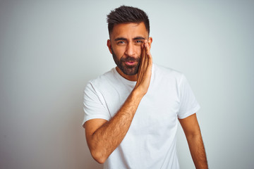 Young indian man wearing t-shirt standing over isolated white background hand on mouth telling secret rumor, whispering malicious talk conversation